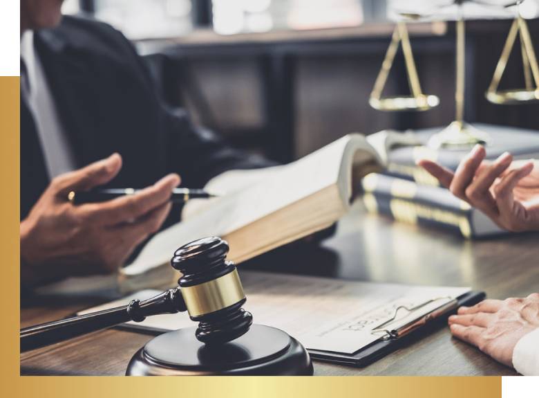 Person holding book and pen, with gavel, documents, balance scale, and another's hand visible